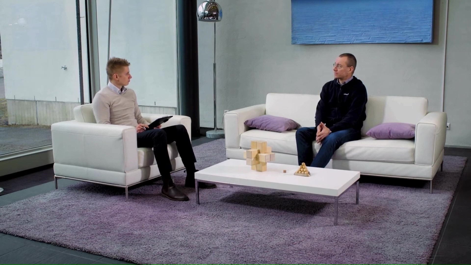 Kaksi miestä istuu valkoisilla sohvilla huoneessa keskustelemassa ERP-järjestelmistä ja Microsoftin pilviratkaisuista.